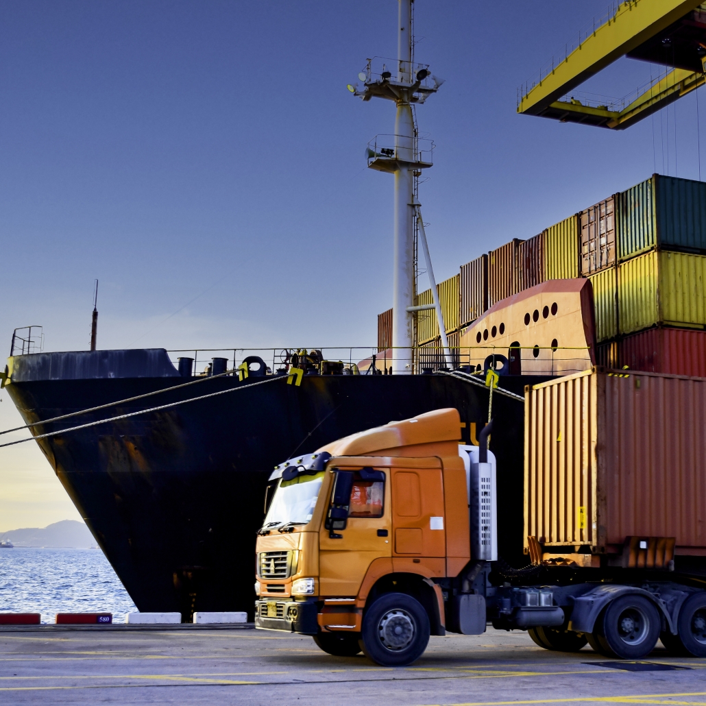 Truck carrying forty-foot container leaving port terminal with ship and quay crane on the background Seaport operation activities container shipping and logistics